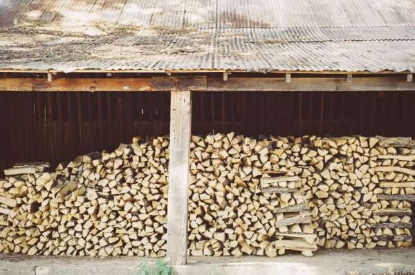 A neatly stacked pile of firewood under a rustic shed with a corrugated metal roof.